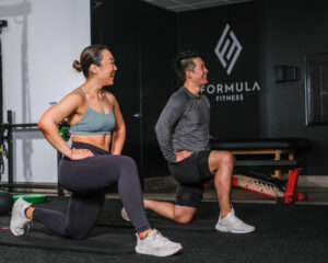 Couple in a low lunge getting direction from their personal trainer