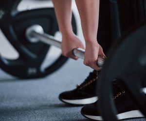 Cropped photo of woman doing squatting with barbell in the gym.